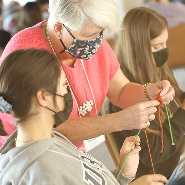 Dr. Kerry Renwick (centre) helps two female students knit tiny orange sweaters at Indigenous Teachers Education Program – NITEP Day, September 24, 2021