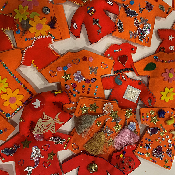 tiny, orange felt shirts decorated with flowers, hearts, beads, maple leaves, and animals.